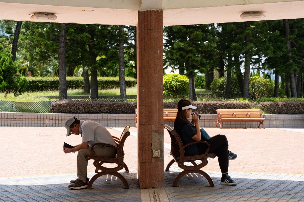 A man and woman sit on benches taking shade from the sun during a Hong Kong heatwave.
